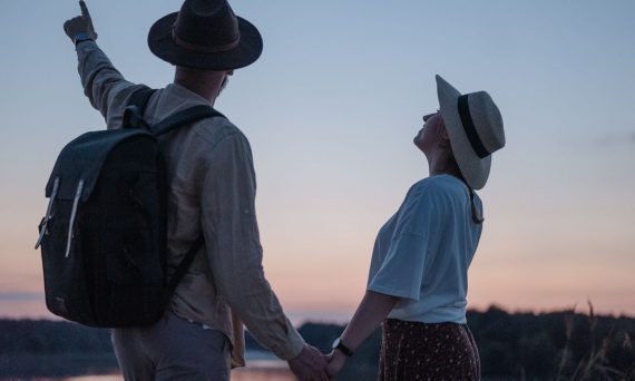Romantic couple holding hands while watching a sunset at a serene lakeside location, embracing nature.